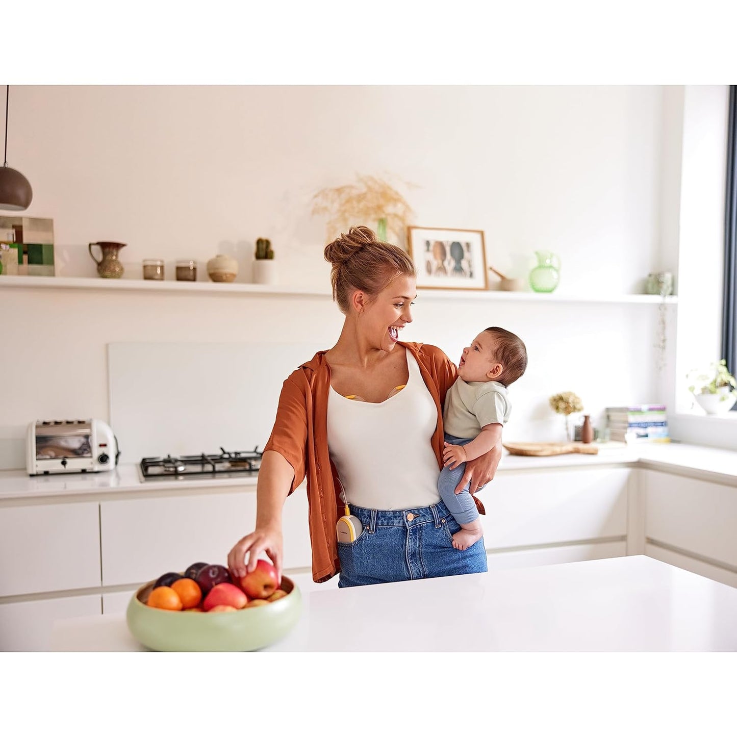 Mom holding baby while wearing Medela Hands-Free Collection Cups, showcasing convenience and comfort.