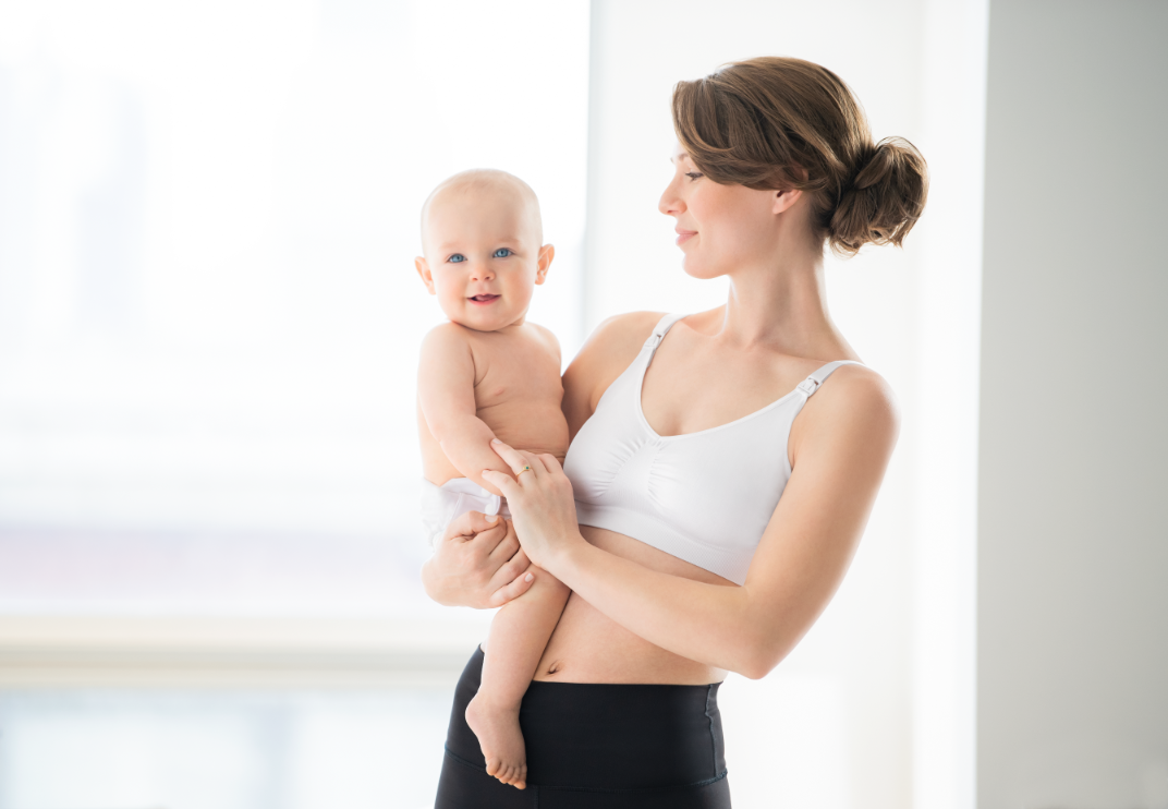 Woman holding baby while wearing Medela nursing bra white, showing front design.