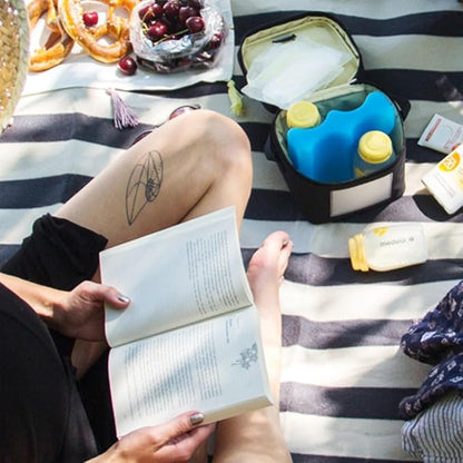 Mom reading a book with Medela Cooler Bag placed beside her for convenient breast milk storage.