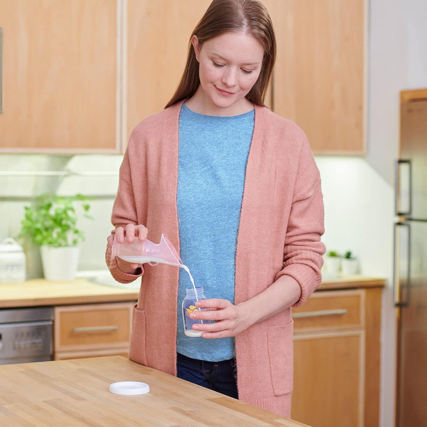 Mom using Medela Silicone Breast Milk Collector to transfer milk into a bottle