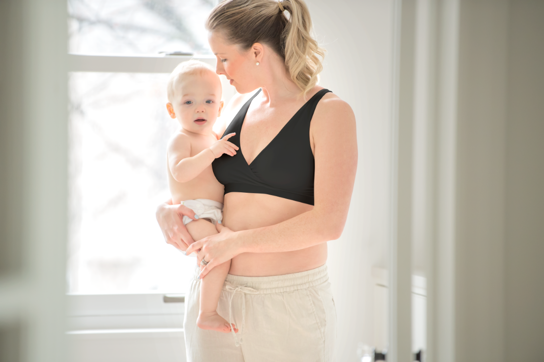 Mom wearing Medela black sleep bra while holding her baby