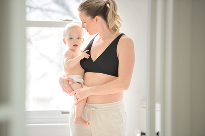 Mom wearing Medela black sleep bra while holding her baby