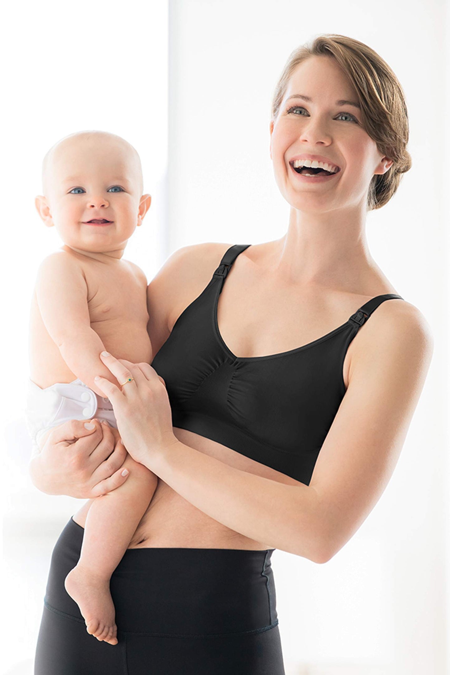 Woman holding baby while wearing black Medela Comfy Bra, showing front design.