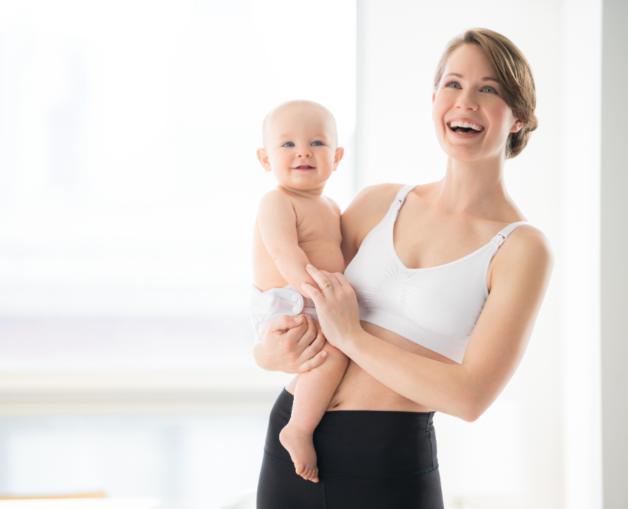 Woman holding baby while wearing white Medela nursing bra, showing front design.